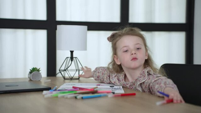 baby girl draws while sitting at table by the window at home. happy family kid concept. baby daughter learns to draw with pencils on a sheet of paper indoors. development of fine dream motor skills