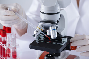 A scientist is using a microscope to examine a blood sample. Test tubes with blood in laboratory. Blood HIV test. - 780040432