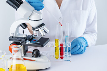 Female biotechnology scientist working in laboratory with chemical liquid. Scientist is researching in laboratory, test tubes with liquid and microscope.  - 780040457