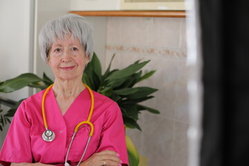Senior female nurse wearing pink scrubs and yellow stethoscope 