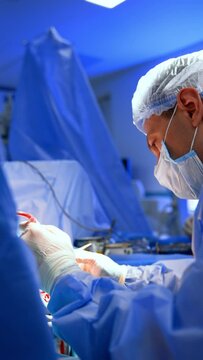 Confident attentive surgeon in mask and cap performs surgery. Side view portrait of a professional using tools. Vertical video.