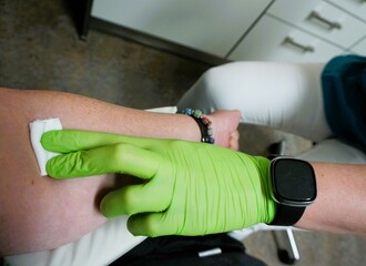 Ärztin mit grünen medizinischen Gummihandschuh drückt weißen Wattepad auf Arm von Patientin...