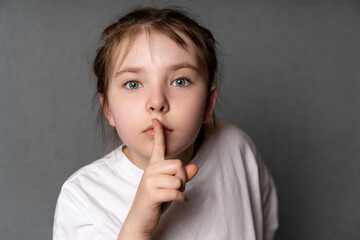 Fototapeta premium Portrait of a little cute teenage girl showing a sign of silence with a finger to her mouth. The Girl Has a Secret. High quality photo