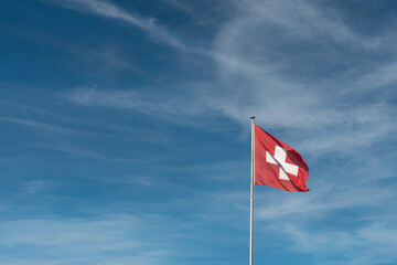 Flag of Switzerland, Europe on a pole waving in the wind. Large copy space on the left. Swiss cross