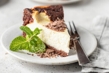 Piece of homemade chocolate cheesecake topped with chocolate chips mint leave on a plate close up on white textured background