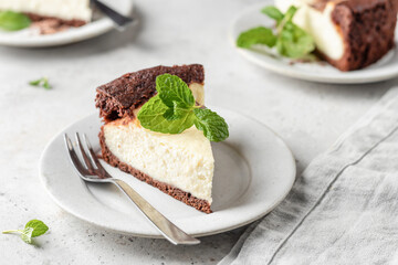 Piece of homemade chocolate cheesecake with mint leave on a plate on white textured background