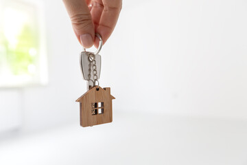Home key in hand at empty room with new flat background inside new house. Real estate and moving concept. White copy space.