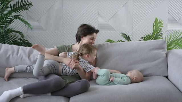 Affectionate loving young mom enjoying tender moment with sweet cute little kid daughter sitting on cozy grey couch at home. Happy caring mother spending time with laughing small baby in living room