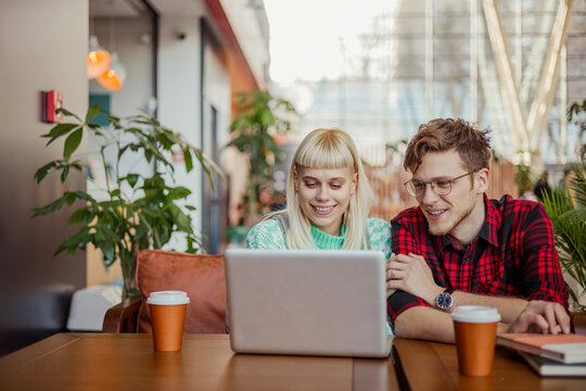 Digital nomads sitting in cafe with a laptop and smiling at it. - Powered by Adobe
