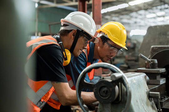 Man worker in safety helmet working on steel machine. Smart factory worker using machine in factory workshop. - Powered by Adobe