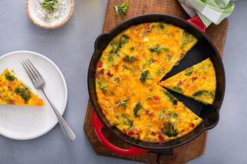 Healthy frittata or quiche with broccoli and red pepper cut in a cast iron pan