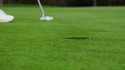 Close shot at ground level of a golfer on a carefully maintained putting green, the golfer putts the golf ball but misses the hole. - Powered by Adobe
