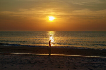 Silhouette of a man running along the sandy beach on the seashore against the backdrop of the setting sun