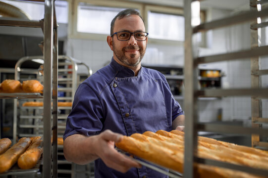 Man baker with trays of fresh bread in bakery.