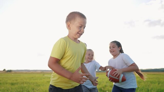 children playing rugby in the park. a group of children play american lifestyle football run outdoors in the park in summer. happy family kid dream concept. family children play american football run