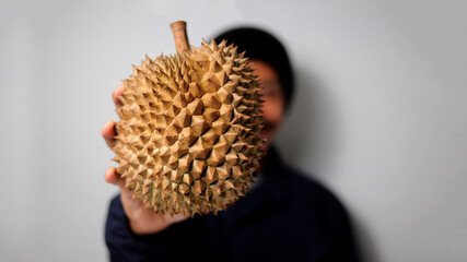 Asian man smiles while holding a spiky durian on white background.