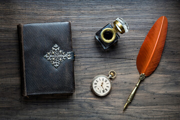 Old quill pen, old book, clock and vintage inkwell on wooden desk in the old office . Retro style. Conceptual background on history, education, literature topics. - obrazy, fototapety, plakaty