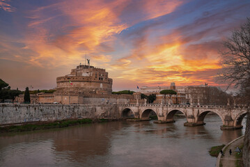 A scenic view of Castel Sant'Angelo and Ponte Sant'Angelo bridge over Tiber River in Rome, Italy. Historical landmarks, river, and cloudy sky with hints of blue.