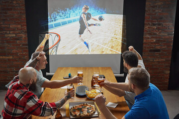 Men, sports enthusiasts gathering to watching online basketball match translation, cheering on...