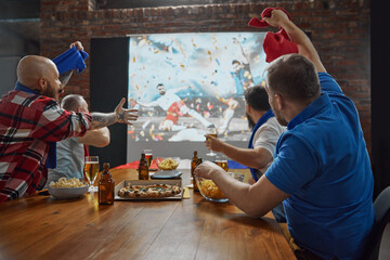 Men emotionally online football match broadcast on TV, cheering for their team while enjoying beer...