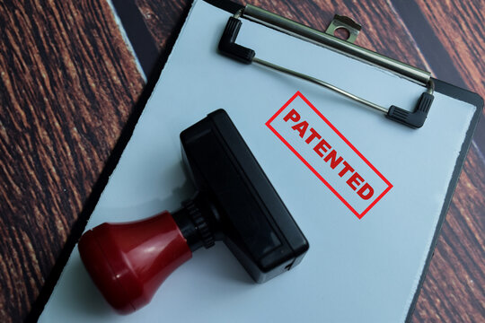 Red Handle Rubber Stamper and Patented text above paperwork isolated on wooden background