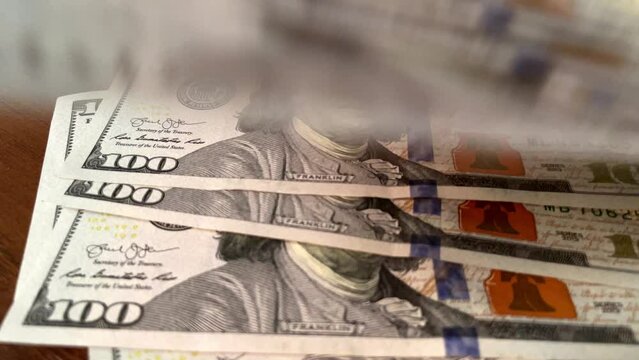 Closeup of hundred dollar bills falling onto wooden table, motion in wealth accumulation