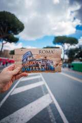 Hand holding illustrated postcard of Colosseum in Rome, Italy with word ROMA and COLOSSEO . Blurred...