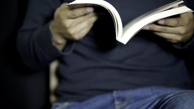 Man Rapidly Flipping Through Book Pages in a Dimly Lit Room at Night