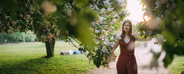 Portrait of a beautiful young woman in the park in the lilac branches at sunset in the summer.