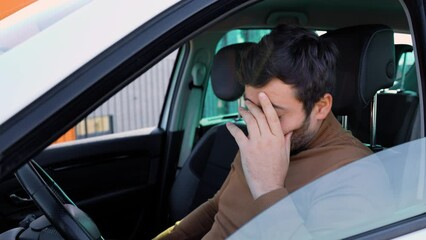 young bearded man has a headache, he holds his head in his hand, he is in the car.