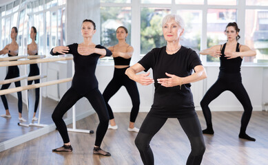 Group of dancers standing in grand plie ballet position in bright fitness room
