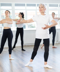 Group of slender women of different ages are learning various dance and ballet movements in the studio