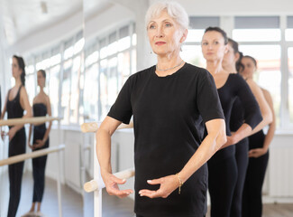 Group of women rehearsing ballet positions at barre in dance studio..