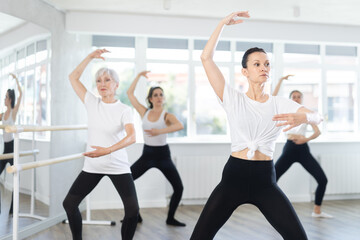 Motivated fit woman, participating in ballet class, practicing basic movements with female group of...