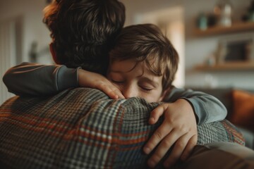 Father hugging son sitting on the sofa in a modern environment, Father's Day concept. - obrazy, fototapety, plakaty