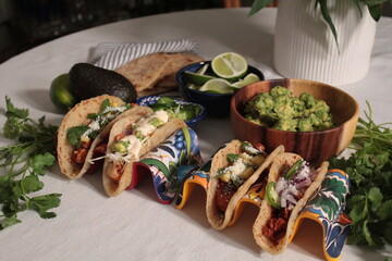 tacos on a table with a bowl of tortillas, limes and guacamole