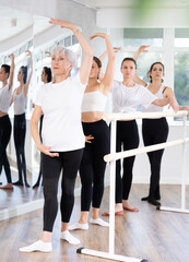 Group of ballerinas preparing for performance, learning and improving quality of rendering stage. Ballerinas near ballet bare repeat forth position with participation experienced mature female mentor