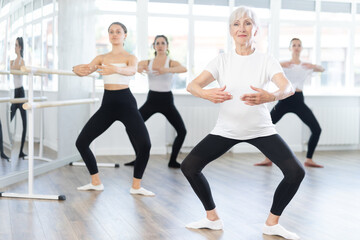 Graceful elderly woman in sportswear confidently leading ballet class with younger female dancers...