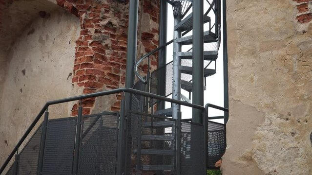 Iron stairs are leading up to the ancient tower. A great example of how historical architecture integrates modern design structures in the form of a metal staircase leading to the castle tower top.