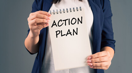 A woman holding a notepad with "action plan" written on it, on a gray background, stock photo