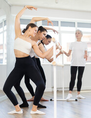 Experienced choreographer teaches ballet dancers movements at ballet barre in a choreographic studio