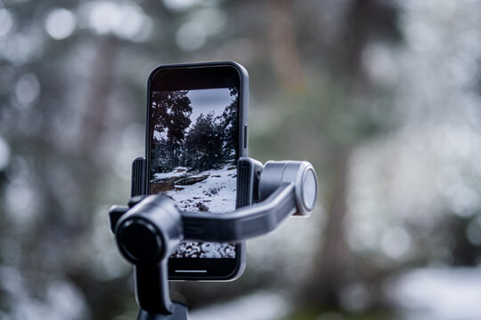 Close-up photo of smartphone capturing landscape with gimbal in snowy forest.