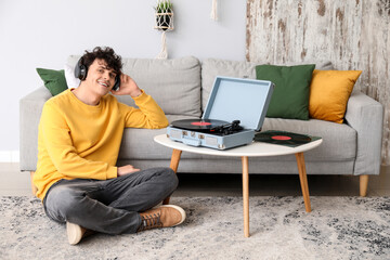 Young man in headphones with record player at home