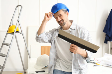Male decorator with putty knife working in room