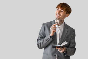 Handsome young tattooed businessman with notebook on grey background