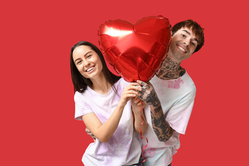 Young couple with heart-shaped air balloon on red background