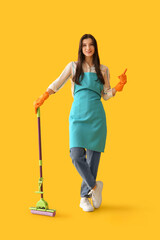 Young woman with floor mop pointing at something on yellow background