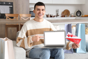 Young man with gift voucher and laptop shopping at home