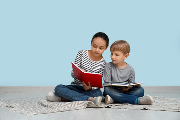 Little children reading books while sitting on floor near blue wall