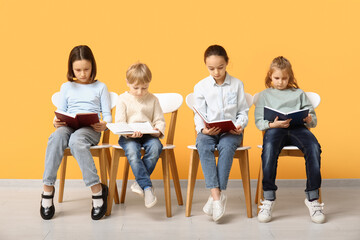 Little children reading books while sitting on chairs near yellow wall